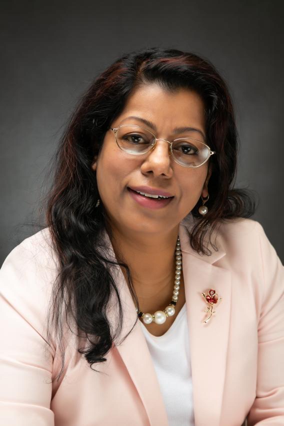 Professional photograph: Smiling woman with glasses, dark hair, and pink blazer.