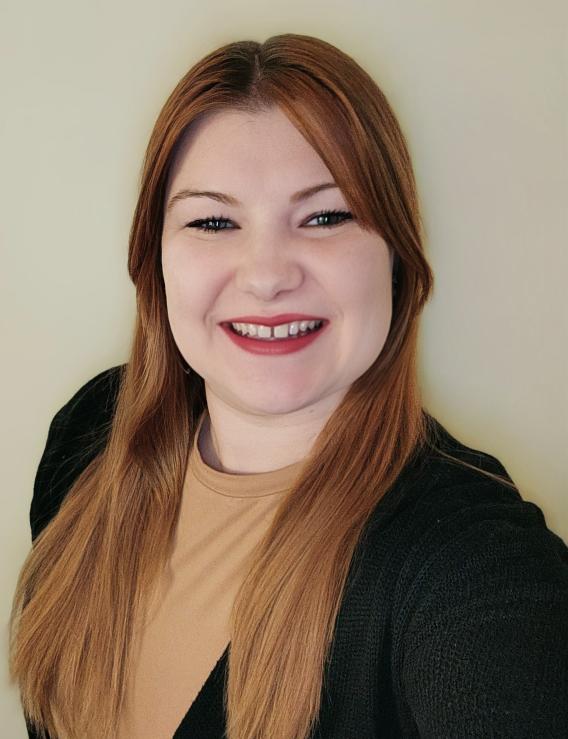 Smiling woman with long, reddish-brown hair and a dark cardigan. Photograph.