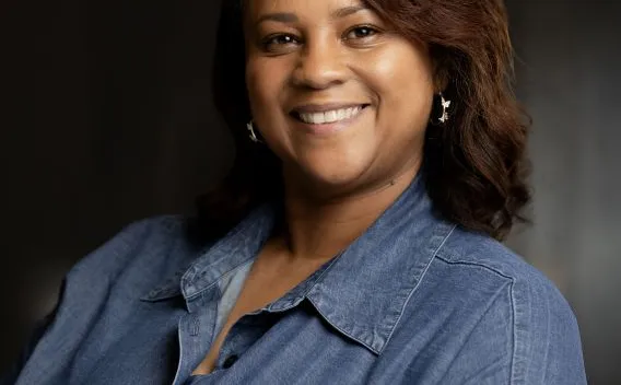 Professional headshot of woman with dark shoulder-length hair, wearing a denim shirt 