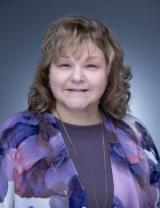 Smiling woman with light brown hair in a purple floral cardigan.