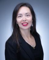 Smiling woman with long dark hair, red lipstick, black jacket against blue-grey background.